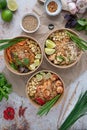 Vertical shot of servings of delicious noodles with salads, lime, greens, seafood, and crumbs