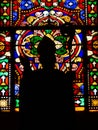 Vertical shot of a silhouette of a clergyman in front of a colorful stained window of a church