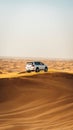 Vertical shot of a silver Jeep parked on a sandy hill in a dessert on a sunny day