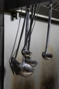 Vertical shot of silver soup ladles on the kitchen on the grey background of wall