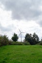 Vertical shot of a single wind turbine surrounded by trees and greenery against the cloudy sky Royalty Free Stock Photo