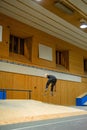 Vertical shot of a skateboarder jumping over the skating ramp inside a building.