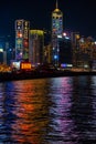 Vertical shot of skyscrapers lighting up Victoria harbor with colorful neon lights in Hong Kong