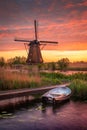 Vertical shot of a small boat in a lake and a mill in the background under the cloudy sunset sky