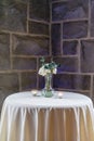 Vertical shot of a small vase with white roses on a small white table in front of a stone wall