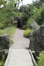 Vertical shot of a small wooden bridge leading to a pavement then a small tunnel, in a park Royalty Free Stock Photo