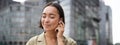 Vertical shot of smiling asian woman in wireless headphones, enjoys listening to music in earphones, holds mobile phone Royalty Free Stock Photo