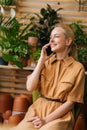 Vertical shot of smiling young woman floral shop owner sitting in floral shop and talking on smartphone with client. Royalty Free Stock Photo