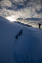 Vertical shot of a snowy hillside with a person trekking and bright sun shining over