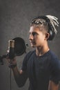 Vertical shot stilysh guy with dreadlocks is recording a song in the studio. A young attractive singer in black studio headphones