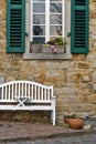 Vertical shot of a stone building facade with flowers, a bench, and green window shutters Royalty Free Stock Photo