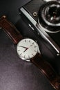 Vertical shot of a stylish wrist watch with an old retro film camera on black background Royalty Free Stock Photo