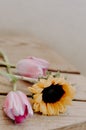 Vertical shot of a sunflower and pink tulips on a wooden table