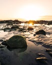 Vertical shot of a sunset over a rocky beach with sunlight reflecting on water Royalty Free Stock Photo