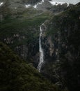 Vertical shot of a tall thin foamy waterfall running down on a grassy rock mountain Royalty Free Stock Photo