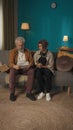 Vertical shot of a teenager, young man sitting with his grandfather on a sofa, couch, reading a document, paper Royalty Free Stock Photo