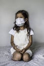 Vertical shot of a thoughtful young Hispanic female with a mask sitting on her bed