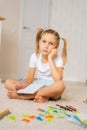 Vertical shot of tired primary little child girl writing homework in notebook sitting on floor at home looking at camera Royalty Free Stock Photo