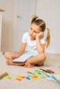 Vertical shot of tired primary little child girl writing looking to laptop screen during homeschooling sitting on floor Royalty Free Stock Photo