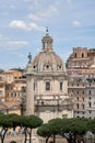 Vertical shot of the titular church with buildings behind a statue on a tower and trees in Rome Royalty Free Stock Photo