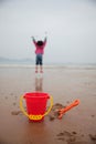 Vertical shot of a toy scapula and a bucket on the sandy beach with a playful kid on the background Royalty Free Stock Photo