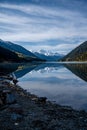 Vertical shot of a tranquil lake reflecting snowy mountains and a cloudy blue sky Royalty Free Stock Photo