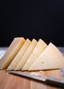 Vertical shot of triangle pieces of cured Manchego cheese and a sharp knife on a wooden food board