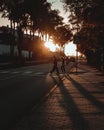 Vertical shot of two friends crossing a road at sunset with the sunlight peeking through trees Royalty Free Stock Photo