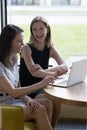 Vertical shot two laughing women sit at table with laptop Royalty Free Stock Photo