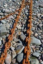 Vertical shot of two old rusty chains on the pebbles on the coast Royalty Free Stock Photo