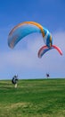 Vertical shot of two persons landing with colorful parachutes on a grassy field