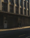 Vertical shot of two persons walking on a sidewalk building