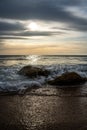 Vertical shot of two rocks on the beach with the beautiful ocean waves at sunset Royalty Free Stock Photo