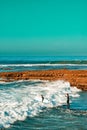 Vertical shot of two surfers walking towards the waves of the beach, carrying their surfboards