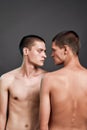 Vertical shot of two young caucasian half naked twin brothers looking at each other while standing isolated over grey Royalty Free Stock Photo