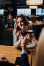 Vertical shot of unrecognizable man and woman clinking glass of red wine with pretty blonde female sitting at table in Royalty Free Stock Photo