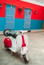 Vertical shot of a vintage Vespa scooter parked in front of a red and blue wall Royalty Free Stock Photo