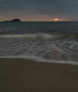 Vertical shot of waves on the coastline with the sun setting in the background