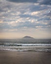 Vertical shot of waves washing the sandy beach with a scenic cloudscape