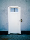 Vertical shot of a white door on a grey wall with a doorbell on the wall Royalty Free Stock Photo