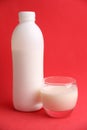 Vertical shot of a white plastic bottle and a glass of milk isolated on a red background Royalty Free Stock Photo