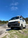 Vertical shot of a white Toyota Hiace Van off-road on sand dune on a blue background