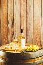 Vertical shot of white wine in glass, bottle, grape and cheese on barrel over wood wall. Royalty Free Stock Photo