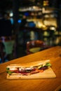 Vertical shot of a whole sandwich with meat, cheese, tomatoes, and lettuce on a wooden board
