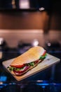 Vertical shot of a whole sandwich with meat, tomatoes, cheese, and lettuce on a wooden board