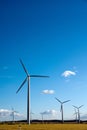 Vertical shot of wind turbines in a field in the countryside under a bright blue sky Royalty Free Stock Photo