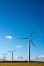 Vertical shot of wind turbines in a field in the countryside under a bright blue sky Royalty Free Stock Photo