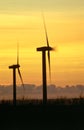 Vertical shot wind turbines silhouetted against the orange sky at sunset