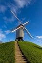 Vertical shot of a windmill situated atop a rolling hillside of lush green grass.