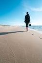 Vertical shot of a woman in dark outdoor clothes with shoes in her right hand, walking barefoot away from the viewer on Royalty Free Stock Photo